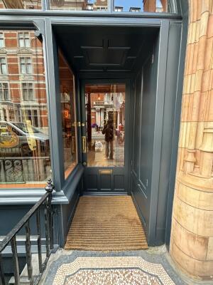 Archway followed by a dark grey wood-framed glass door ahead. Push from handle on left to open.