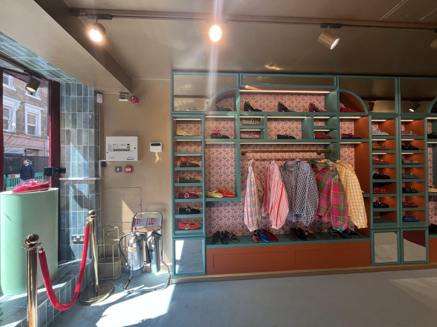 From entrance facing left. Red rope barrier on left. Display shelves with shoes and clothing ahead.