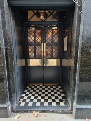 Facing double black glass doors. Push golden pads in centre to open.