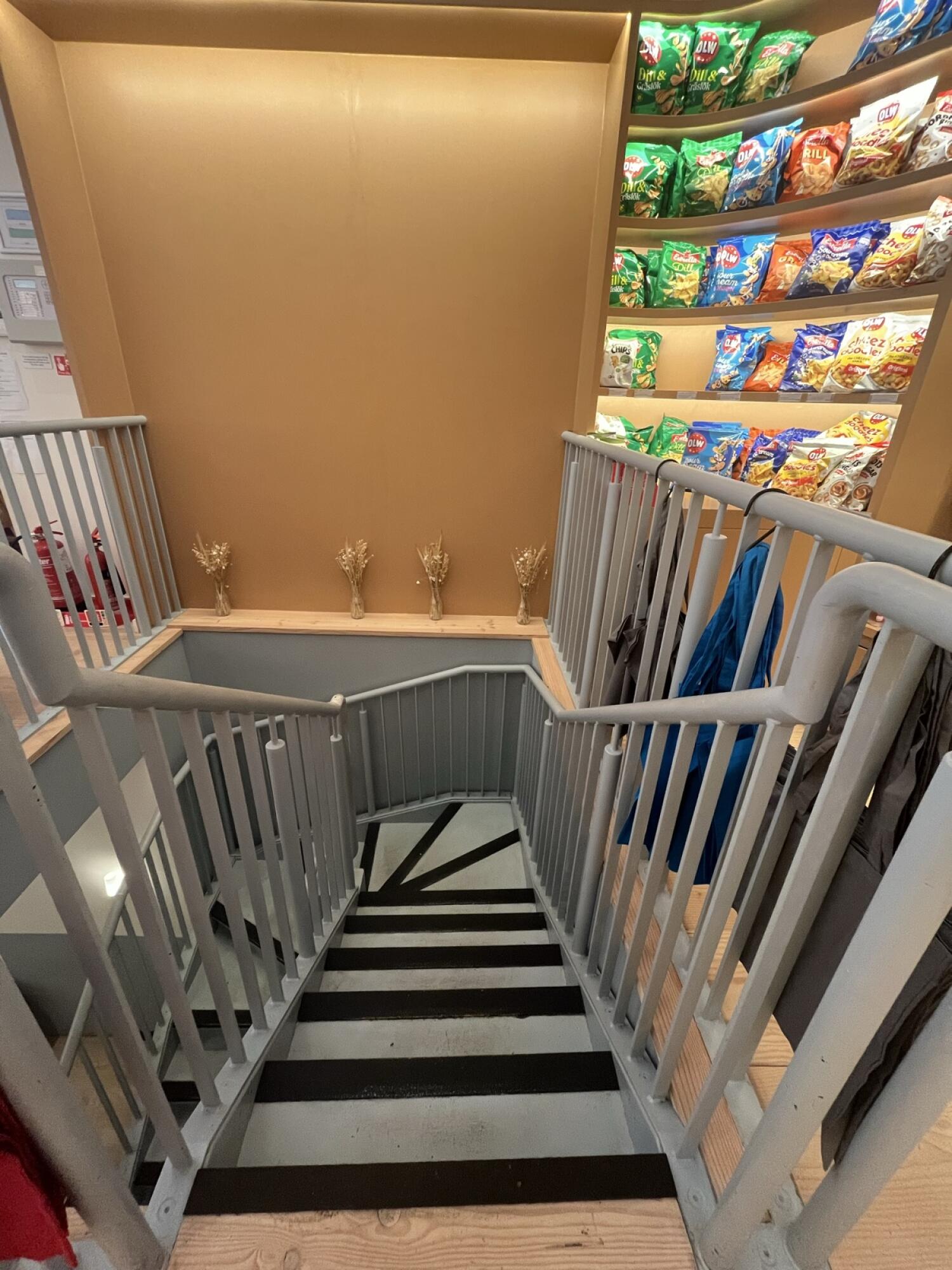 From staircase opening facing straight. Staircase ahead leading down with curve to left. Handrails along left and right.