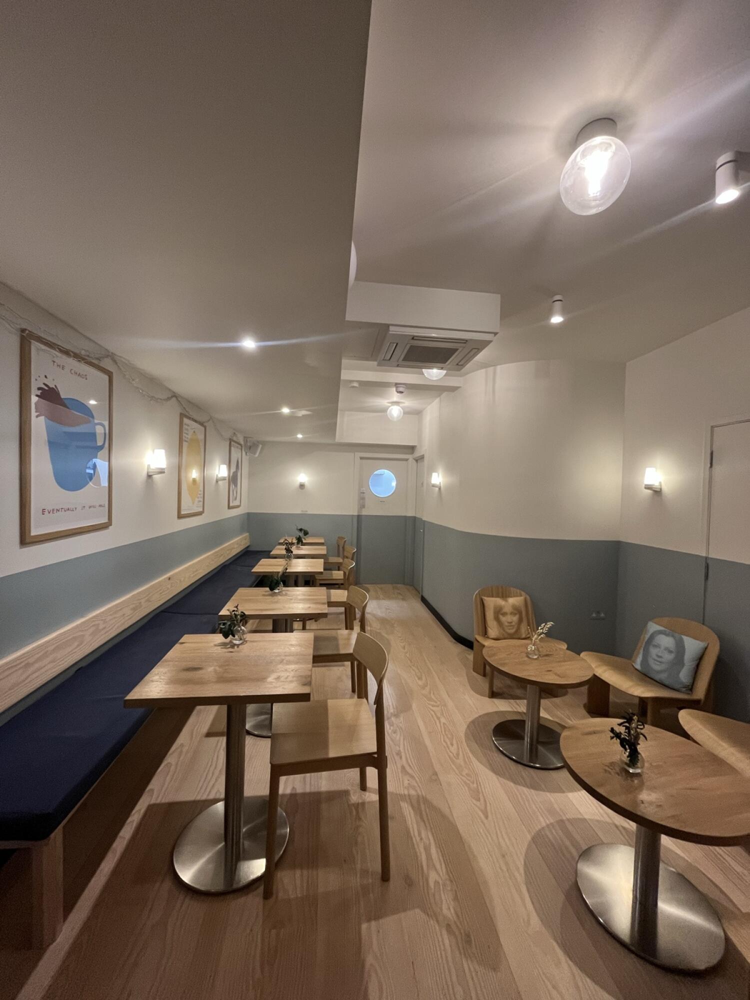 From end of stairs facing right. Half booth along left wall. Row of tables and chairs in centre. Round tables and chairs on right.