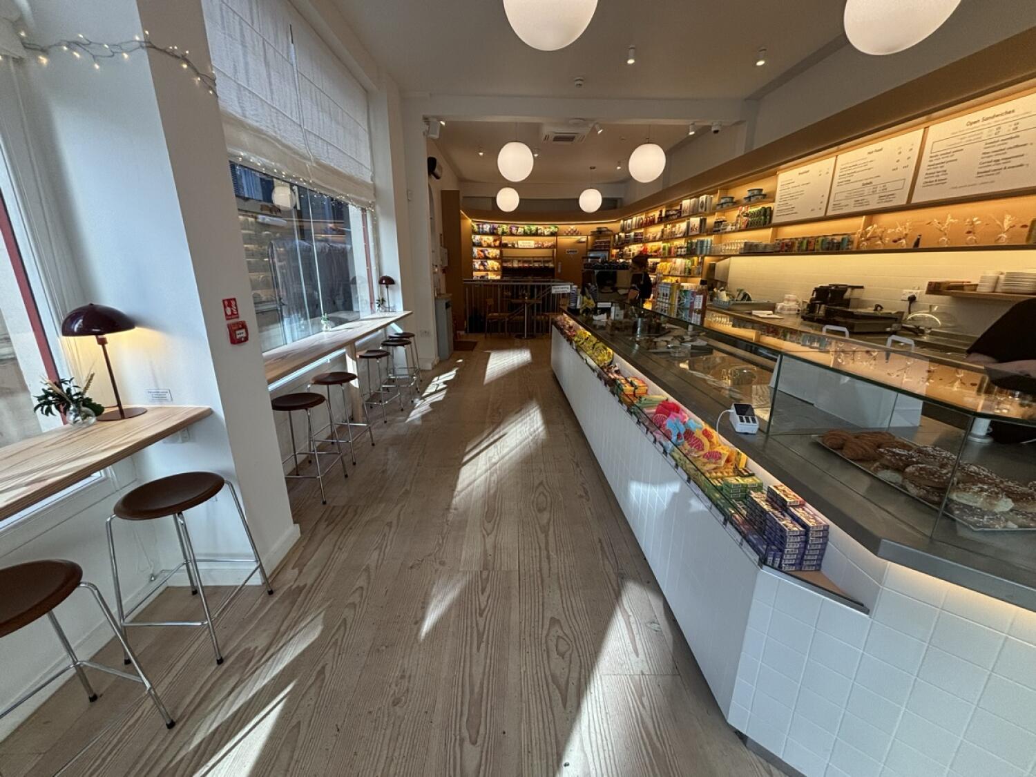 From start of counter facing straight. High tables and stools along left wall. Counter on right. Path ahead to bathroom and downstairs space at back.