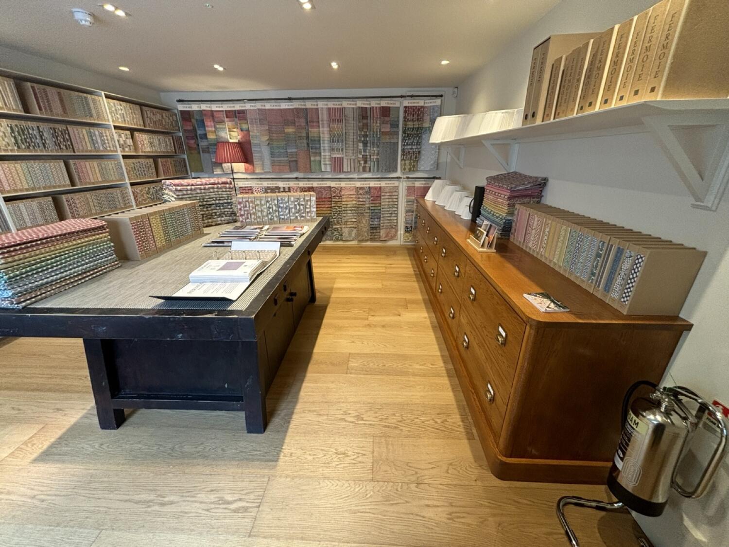 From archway facing right. Product shelves along left and back walls. Central table with product samples on left. Display counter along right wall.