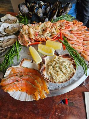 Seafood platter on ice with oysters, mussels, lobster, prawns, salmon, lemon wedges, and samphire.
