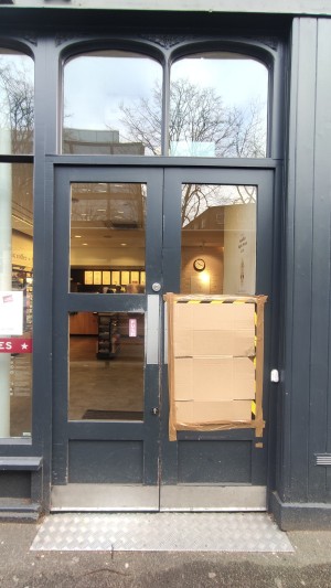 Glass doors with grey frames ahead. Push pads in centre to open.