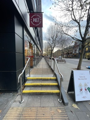From sidewalk along side of venue. Three steps up ahead. Metal handrail along both sides. Entrance on left after landing.
