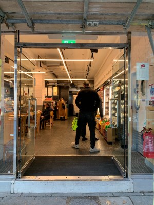 Glass door with silver frame ahead. Push from handle in centre to open. Doorbell on right of door.
