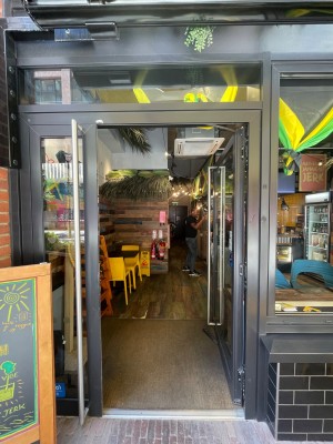 Single glass door with black frame. Push vertical metal handle on left to open.