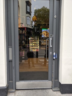 Glass door with grey frame and metal handle on right. Push to open. Doorbell right of door.