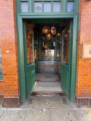 Glass doors with green wooden frame ahead. Push golden metal plaques at center to open.