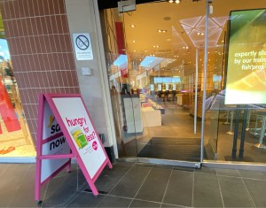 Glass door. Pull metal handle from right to open. A-frame board to left.