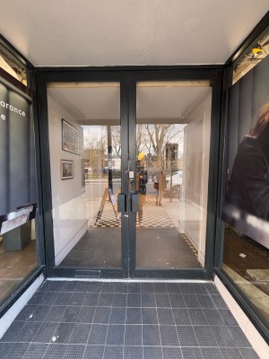 Glass doors with grey frame ahead. Pull metal handles at centre to open.