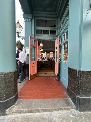 Opening ahead with black and blue pillar on left. Entrance doors at back.