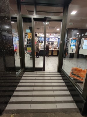 Facing opening to entrance. Built-in ramp ahead going up to black framed glass door.