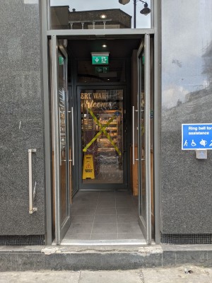 One step up to glass doors with grey frames and metal handles. Push from centre to open. Grab rail left of doors, doorbell right.