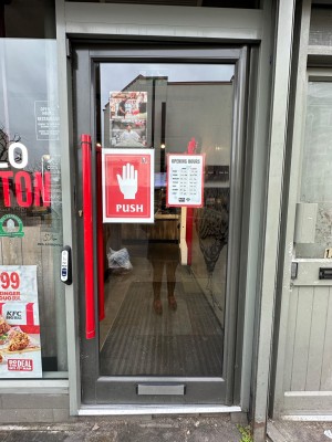 Glass door with red handle on left. Doorbell left of door. Push to open.
