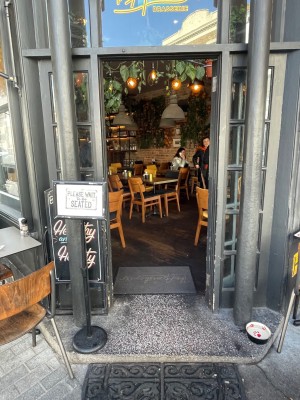 Glass door with grey frame. Push from left to open. Standing sign to left of door.