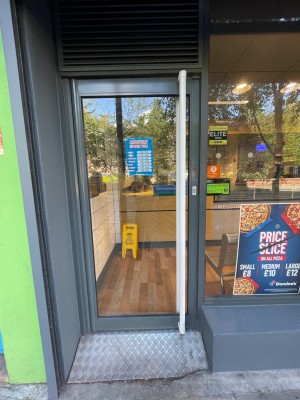 Single glass door with grey frame. Push metal vertical handle on right to open.