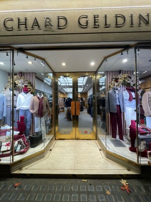 Glass doors with gold frames. Pull or push from centre to open. Glass walls with shop displays to left and right of entrance.