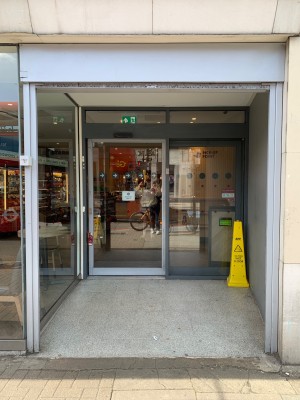 From sidewalk facing venue. Archway ahead. Door at back left.