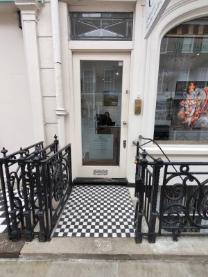 White framed glass door ahead. Push silver handle on right to open. Doorbell for assistance on right of door.