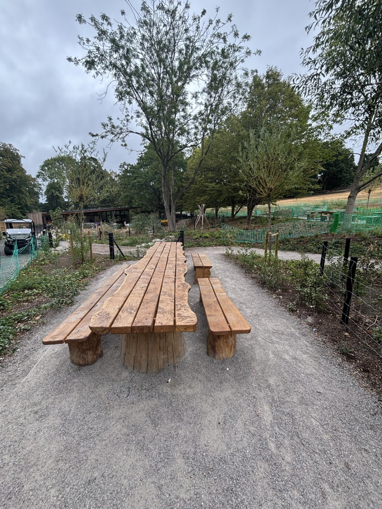 Fenced planting area left. Picnic table on gravel centre. Fenced planting area right.