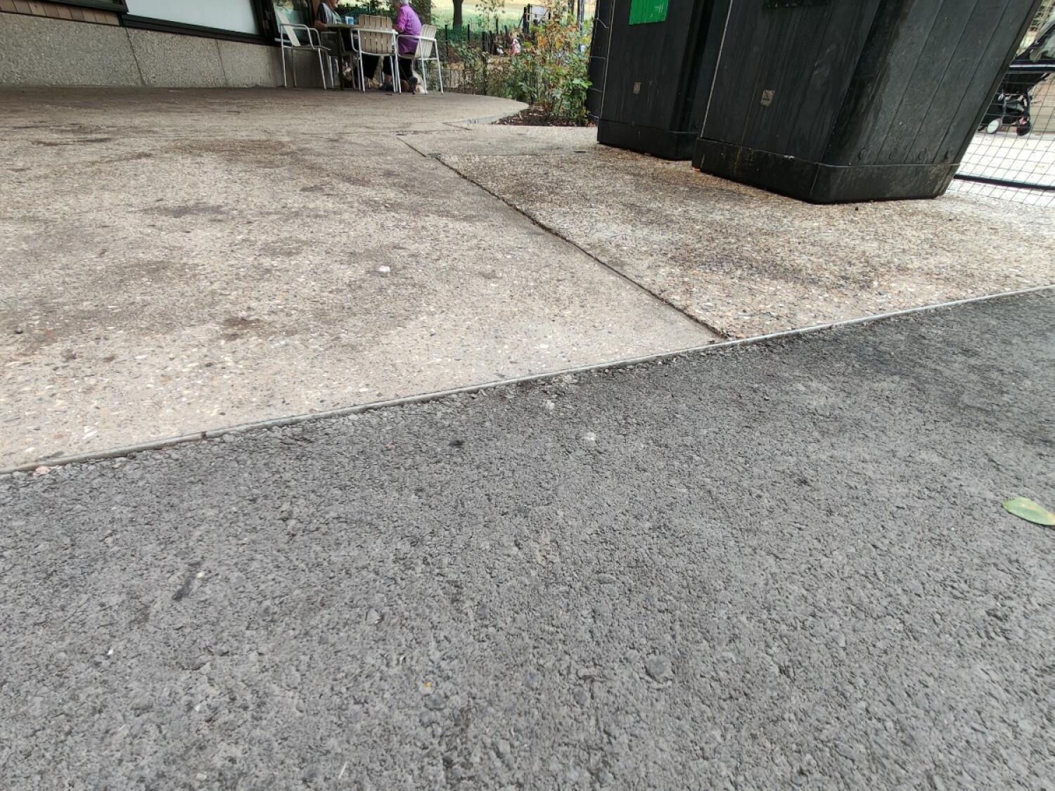 Outdoor seating at back left. Small bump between asphalt and concrete. Black structure on right.