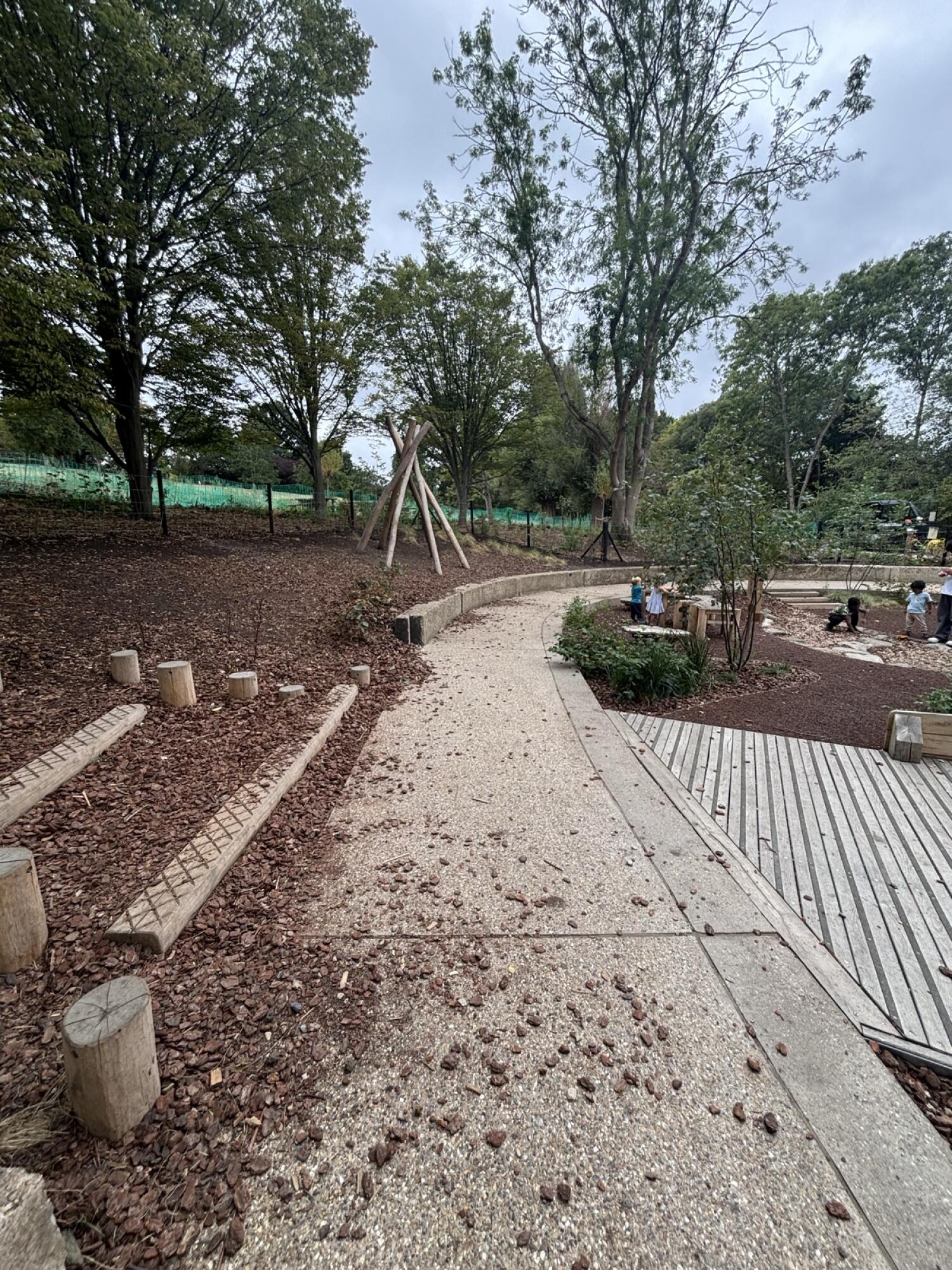 From after fixed benches facing straight. Curved gravel path ahead. Opening on right to play area.