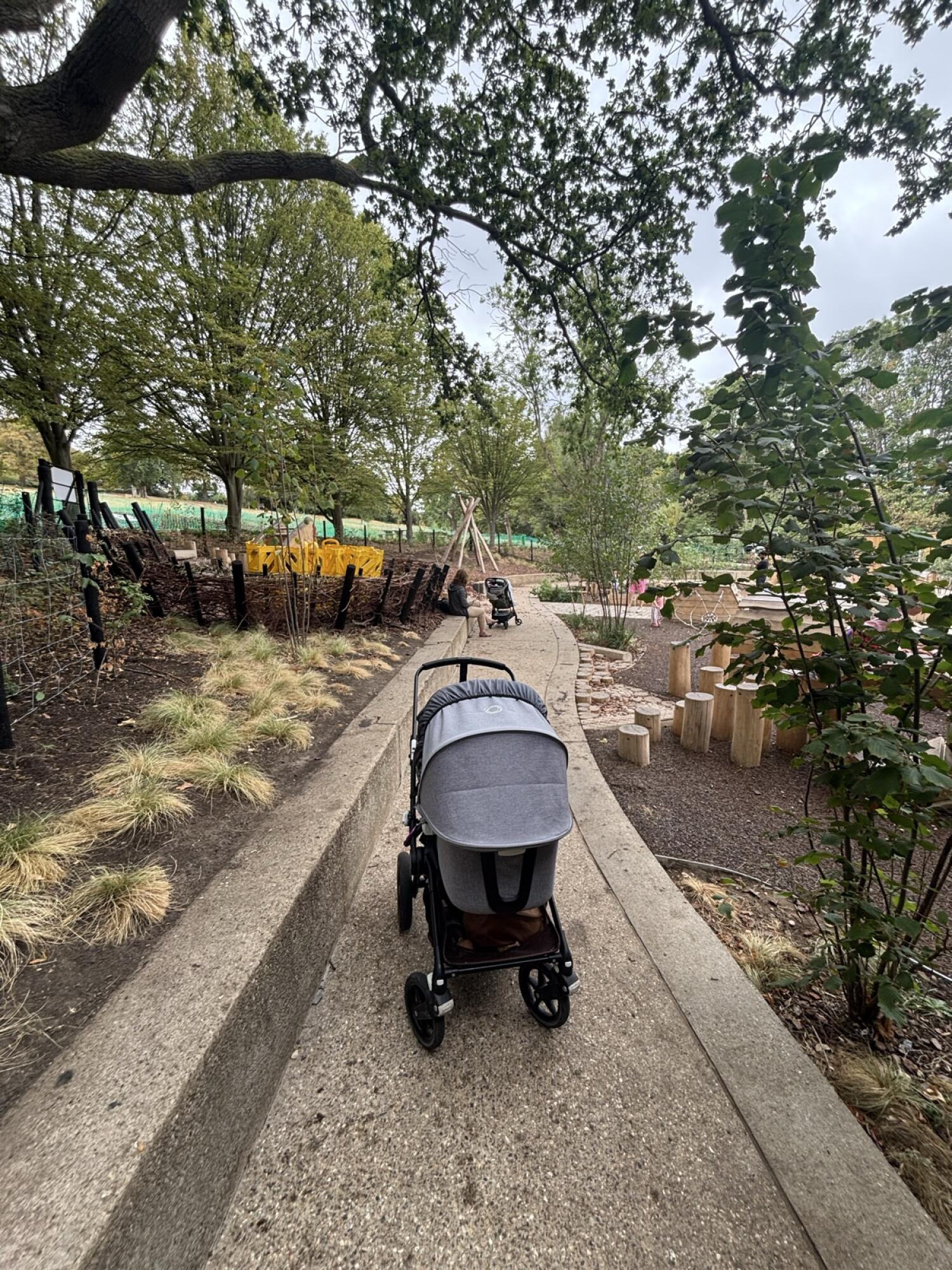 From gate facing straight. Path ahead through outdoor play area. Fixed benches along left of path.