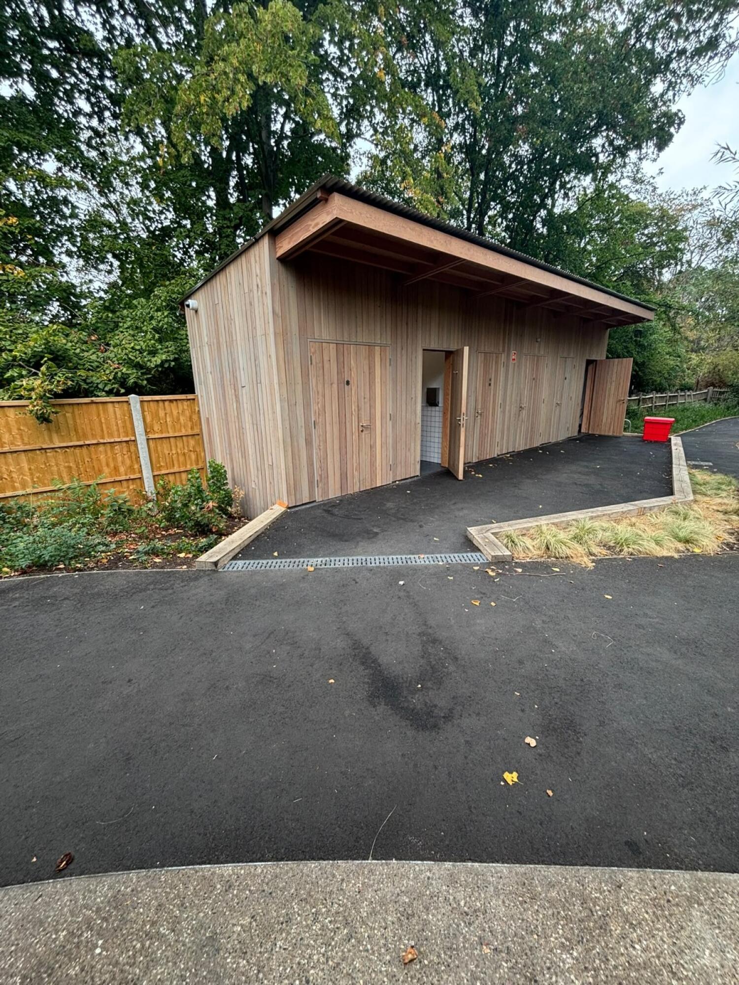 Closed wooden door left. Open doorway in centre. Paved area and doors right.