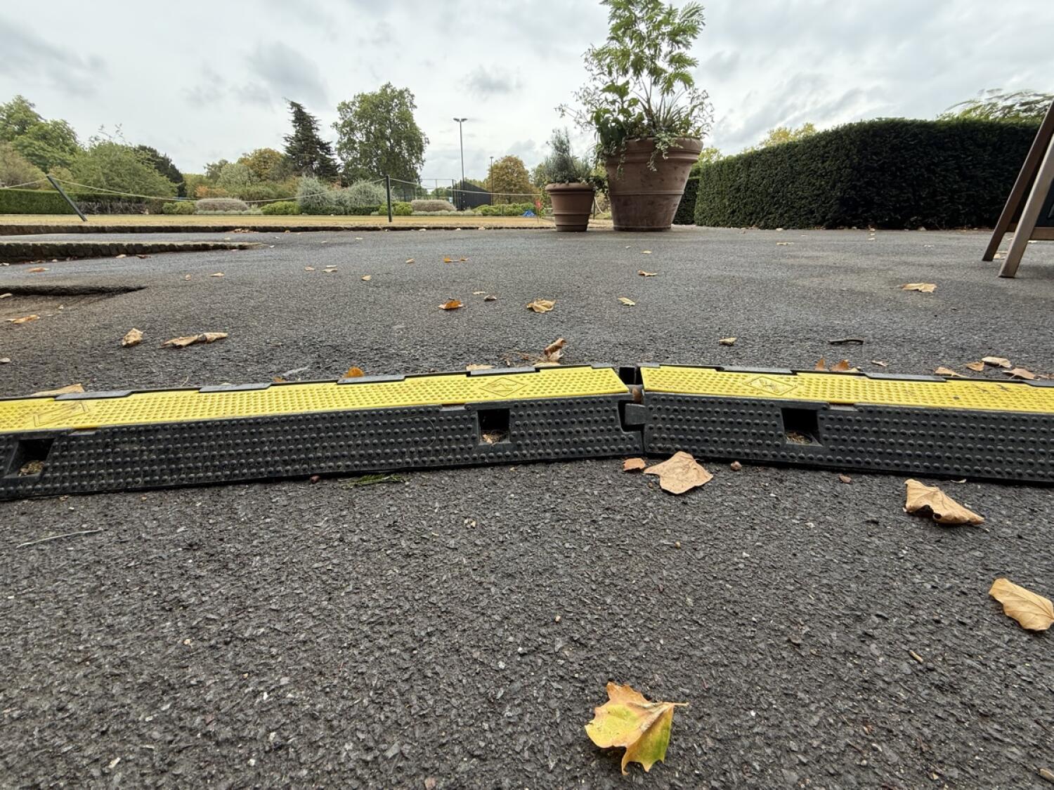 Second raised cable cover across path. Paved outdoor area beyond.