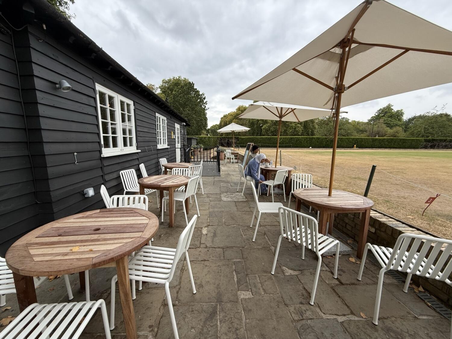 From bottom of ramp facing straight. Tables, chairs and parasols along left and right. Paved path through centre.