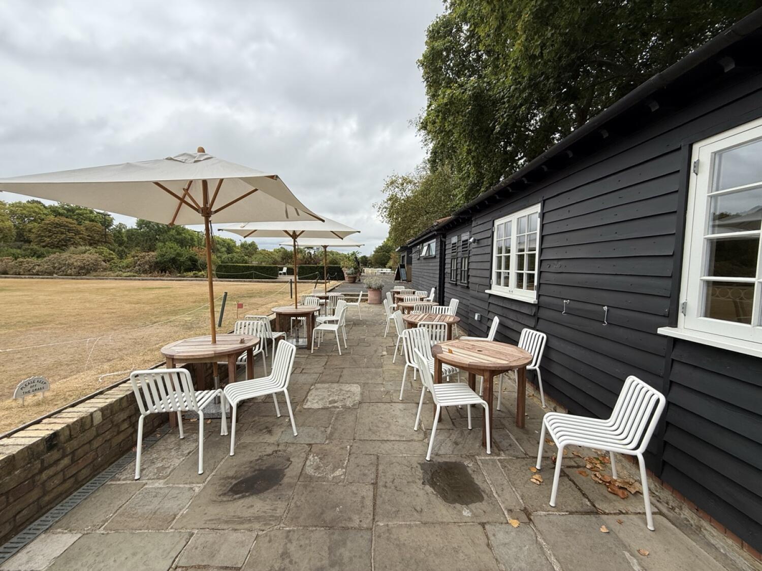 From bottom of ramp facing straight. Tables, chairs and parasols along left and right. Paved path through centre.