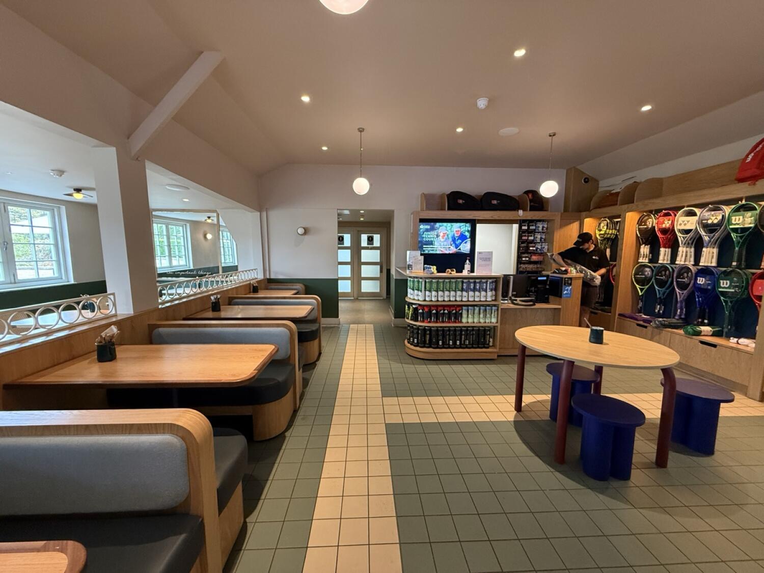 From left of display counter facing straight. Booths along left. Path centre to bathroom. Table and stools on right. Leisure centre counter behind.