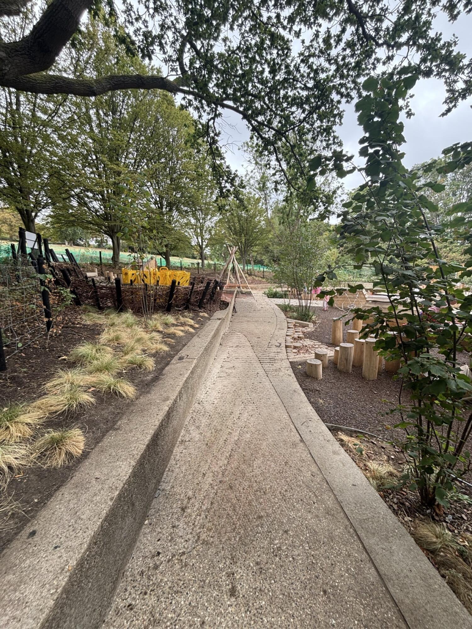 From gate facing straight. Path ahead through outdoor play area. Fixed benches along left of path.