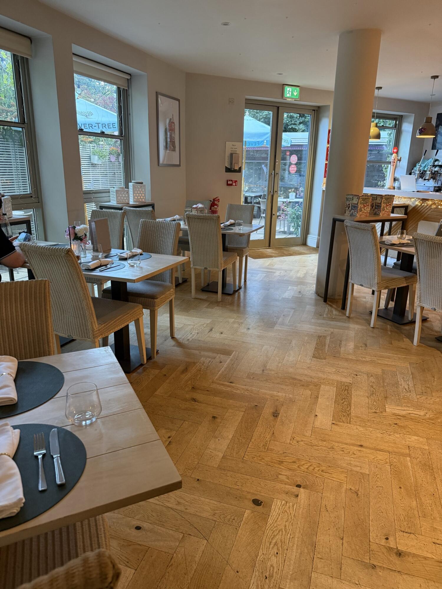 Tables and chairs along left. Entrance doors at back centre. Tables, pillar and counter right.