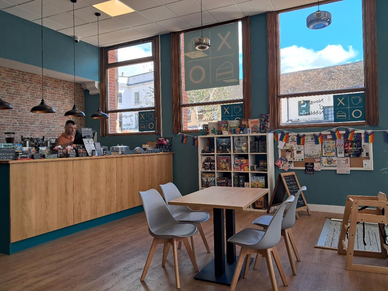 Counter along left wall. Tables and chairs in centre. Product shelves and high chair right.