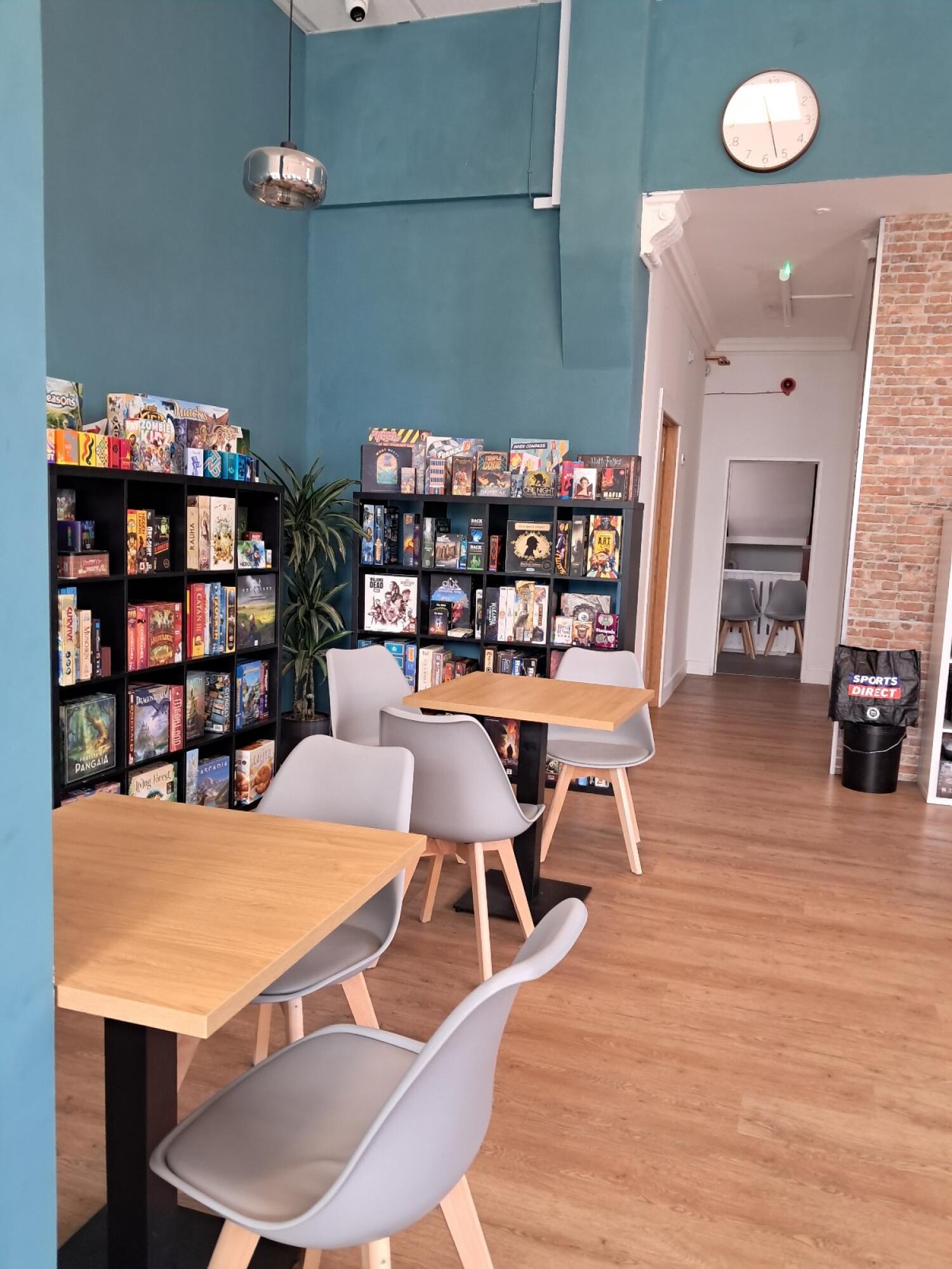 Game shelves along left wall. Tables and chairs in centre. Clear path to back right.