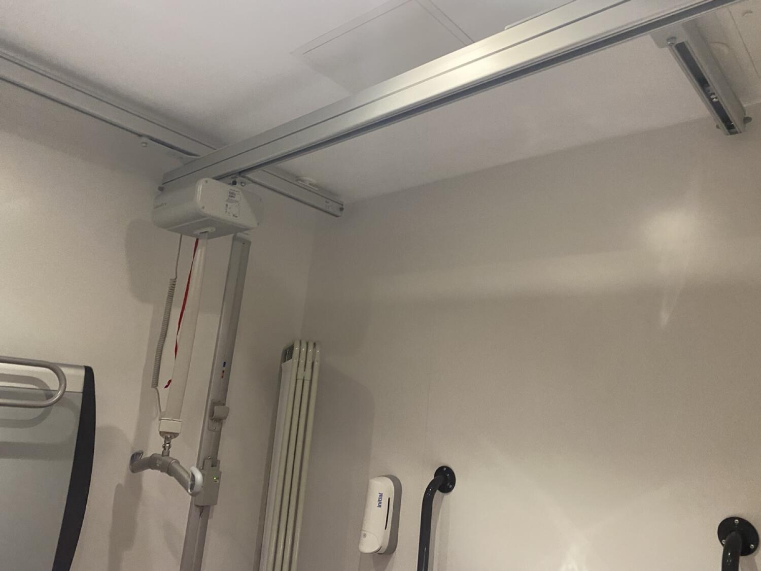 Emergency pull cord on left wall. Ceiling hoist overhead.