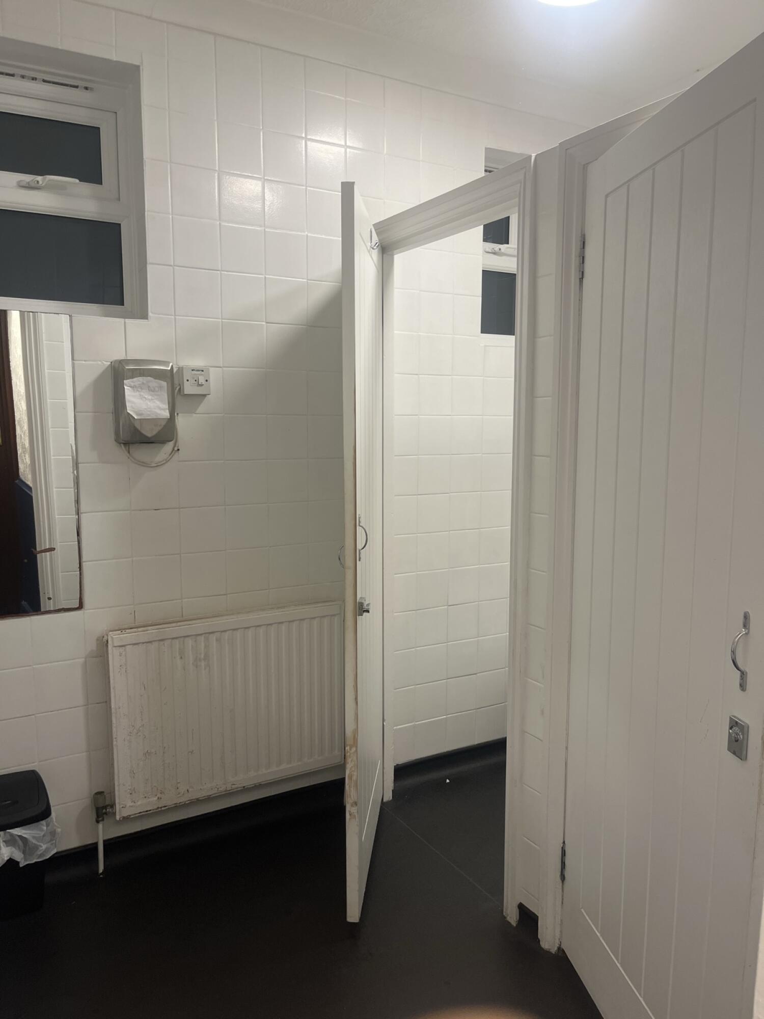 Mirror and radiator on left. Open cubicle door in centre. Closed door on right.