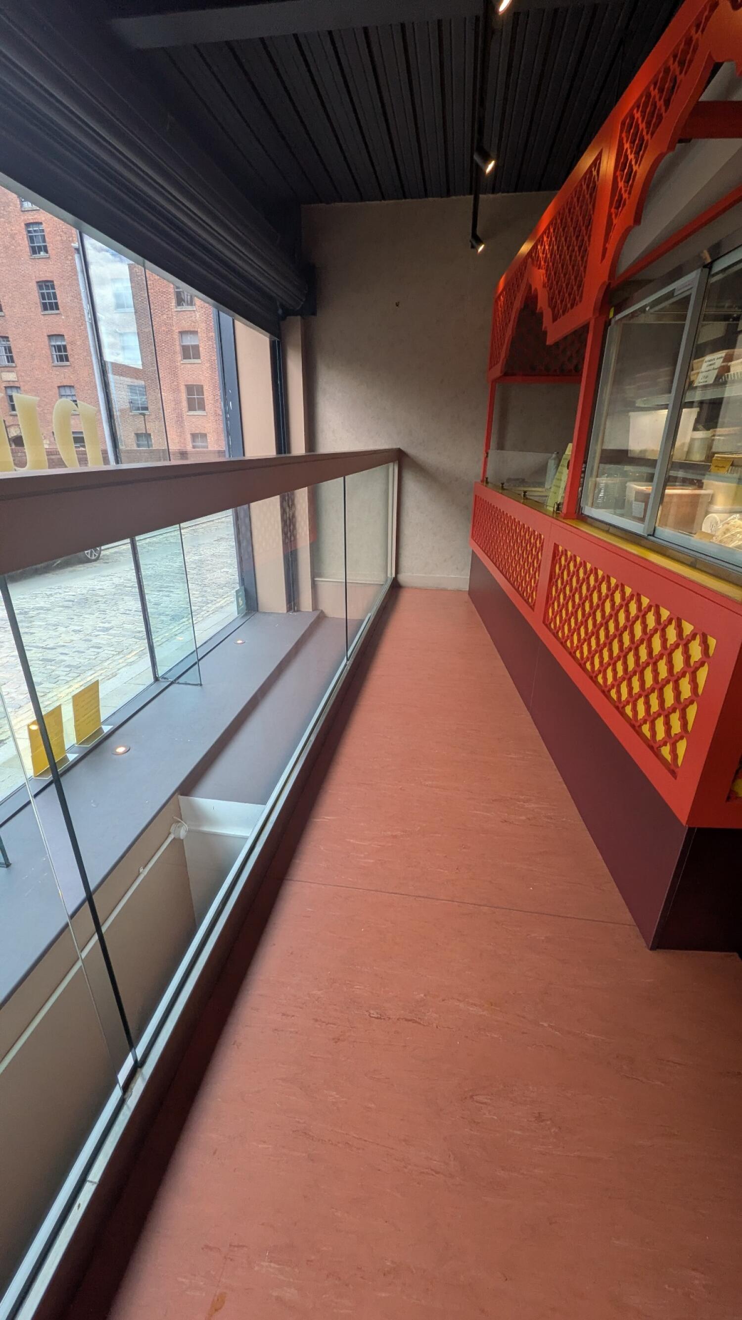 Glass railing along left. Narrow path in centre. Display counter along right.
