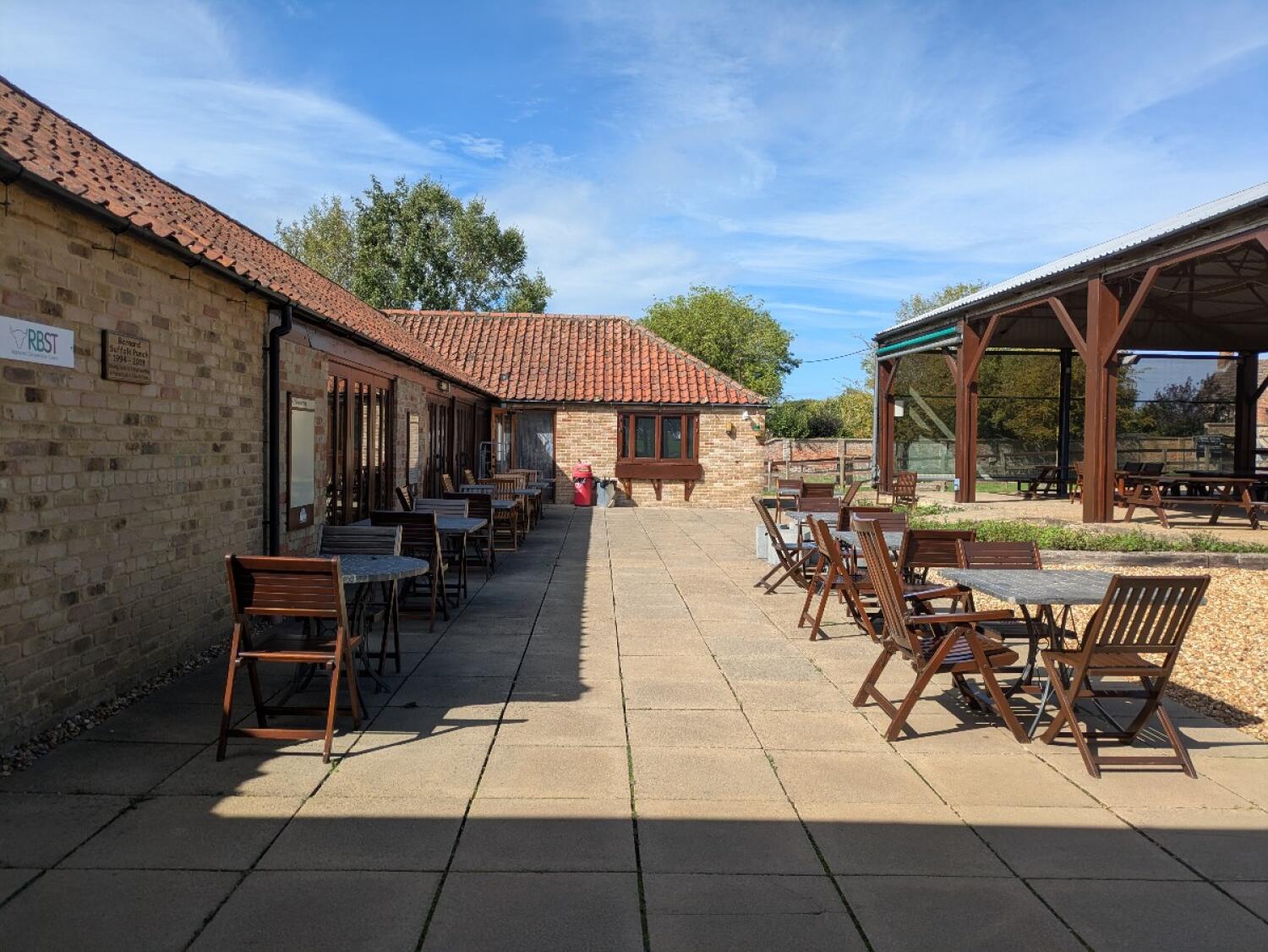 Tables and chairs along left. Paved path through centre. Tables and covered seating right.