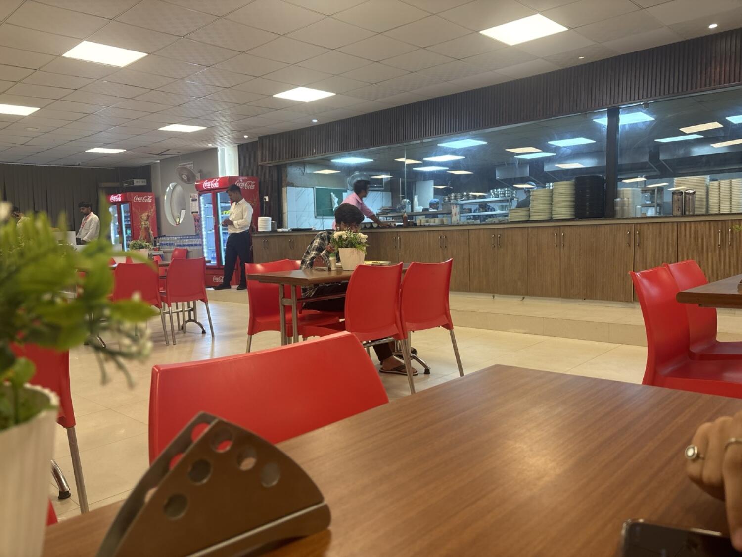 Tables and chairs across dining area. Fridges at back left. Service counter along back right.