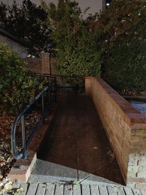 Path ahead with handrail left and brick wall right.