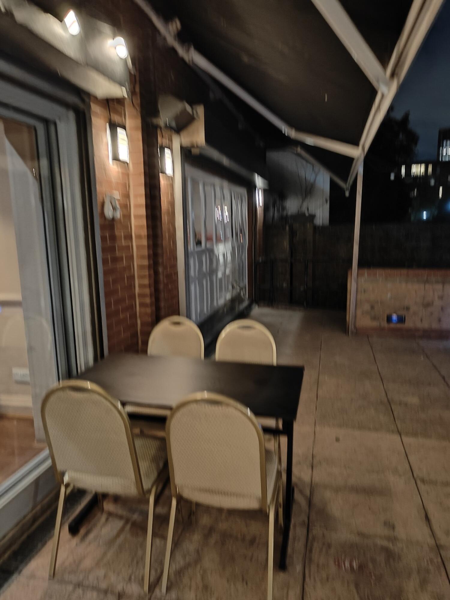 Venue windows along left. Table and chairs in centre. Paved path along right.