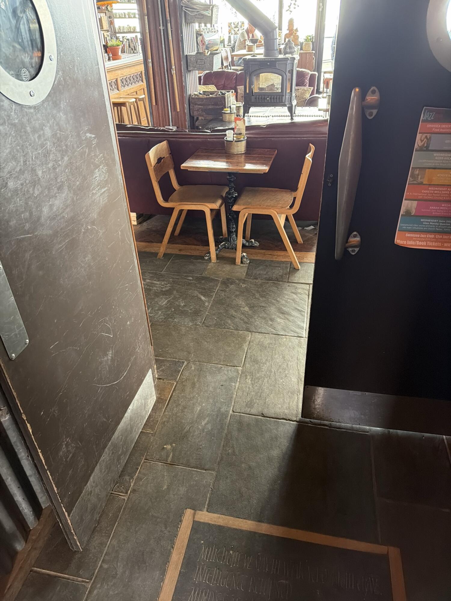 Bar counter along left. Tables and chairs in centre. Open entrance door on right.