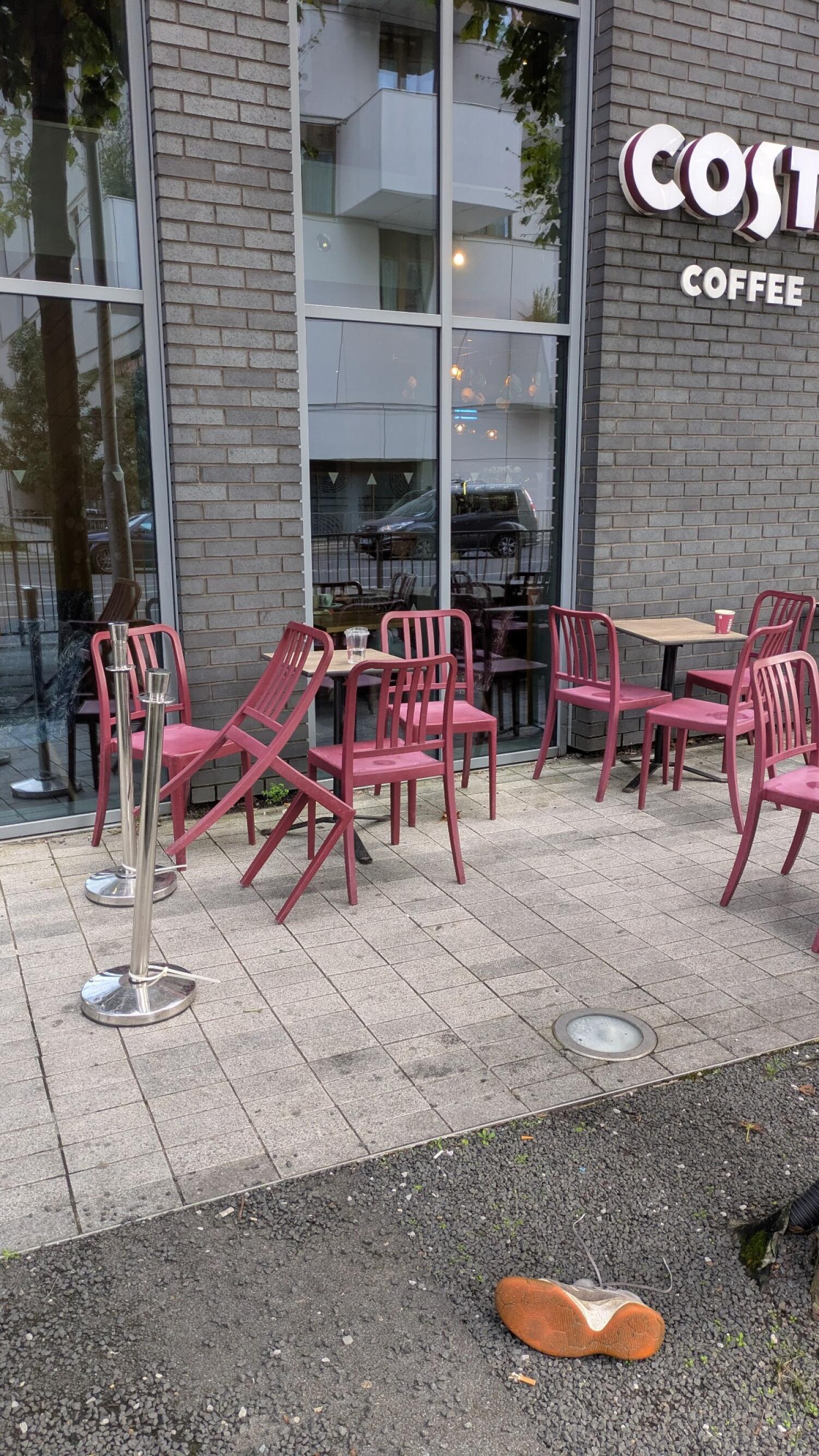 Outdoor tables and chairs along building. Paved seating area with gravel edge.