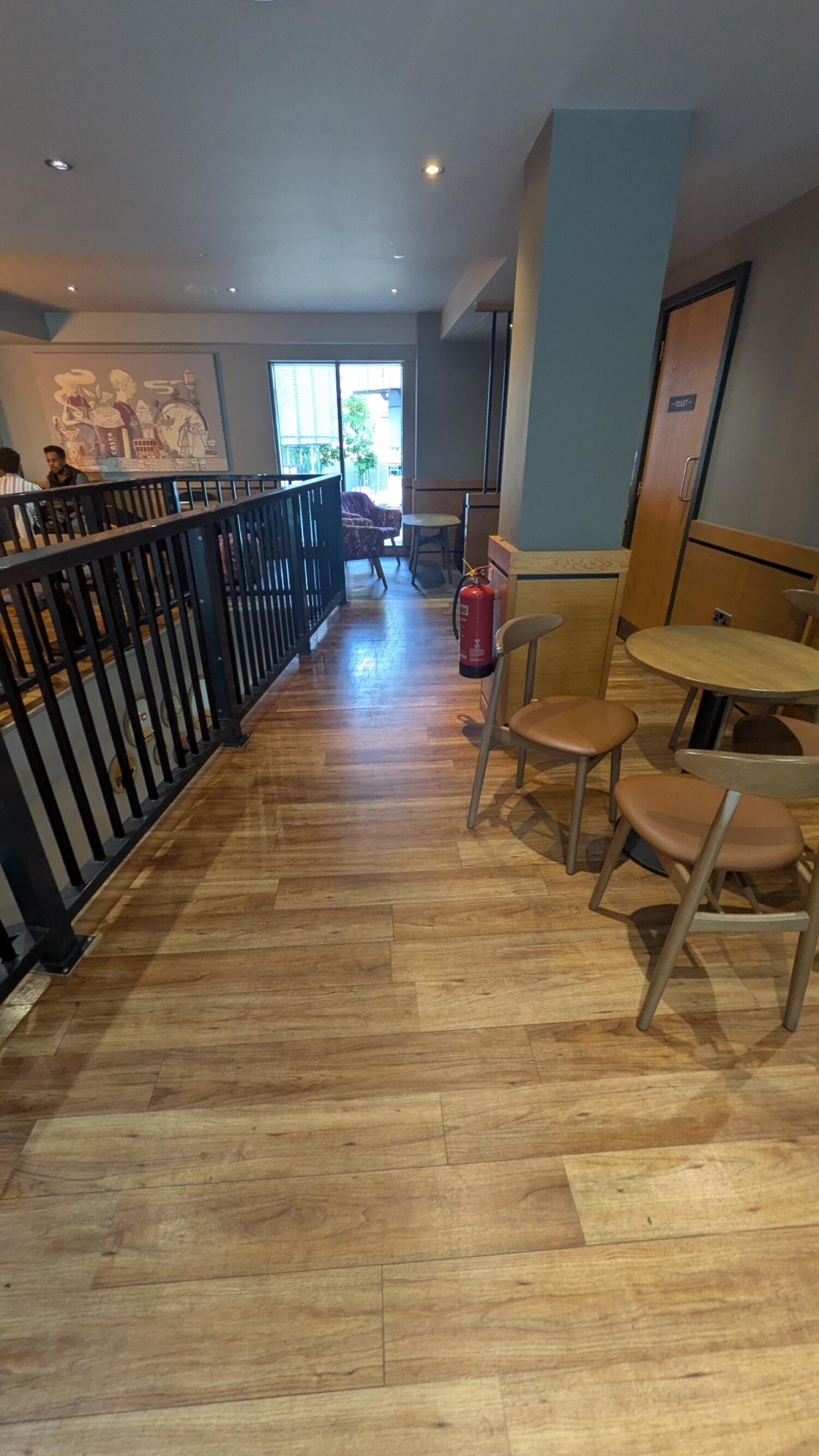 Railing and void along left. Path through centre. Door and tables along right.