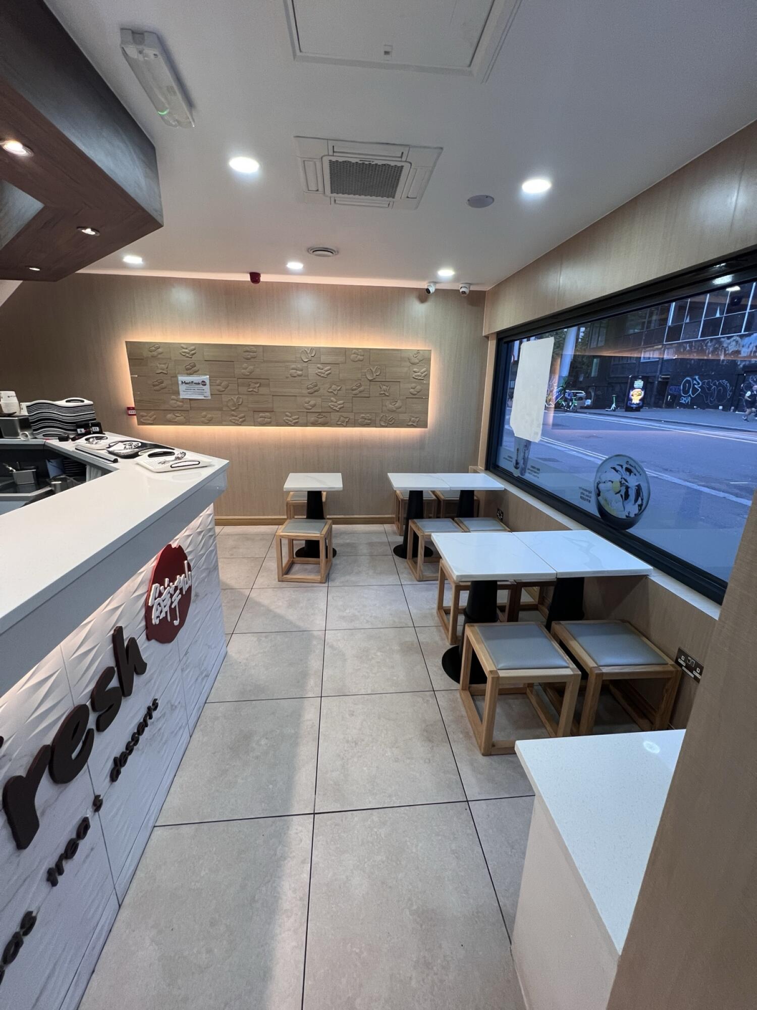 Counter along left. Tables and stools centre and right. Tiled floor throughout.