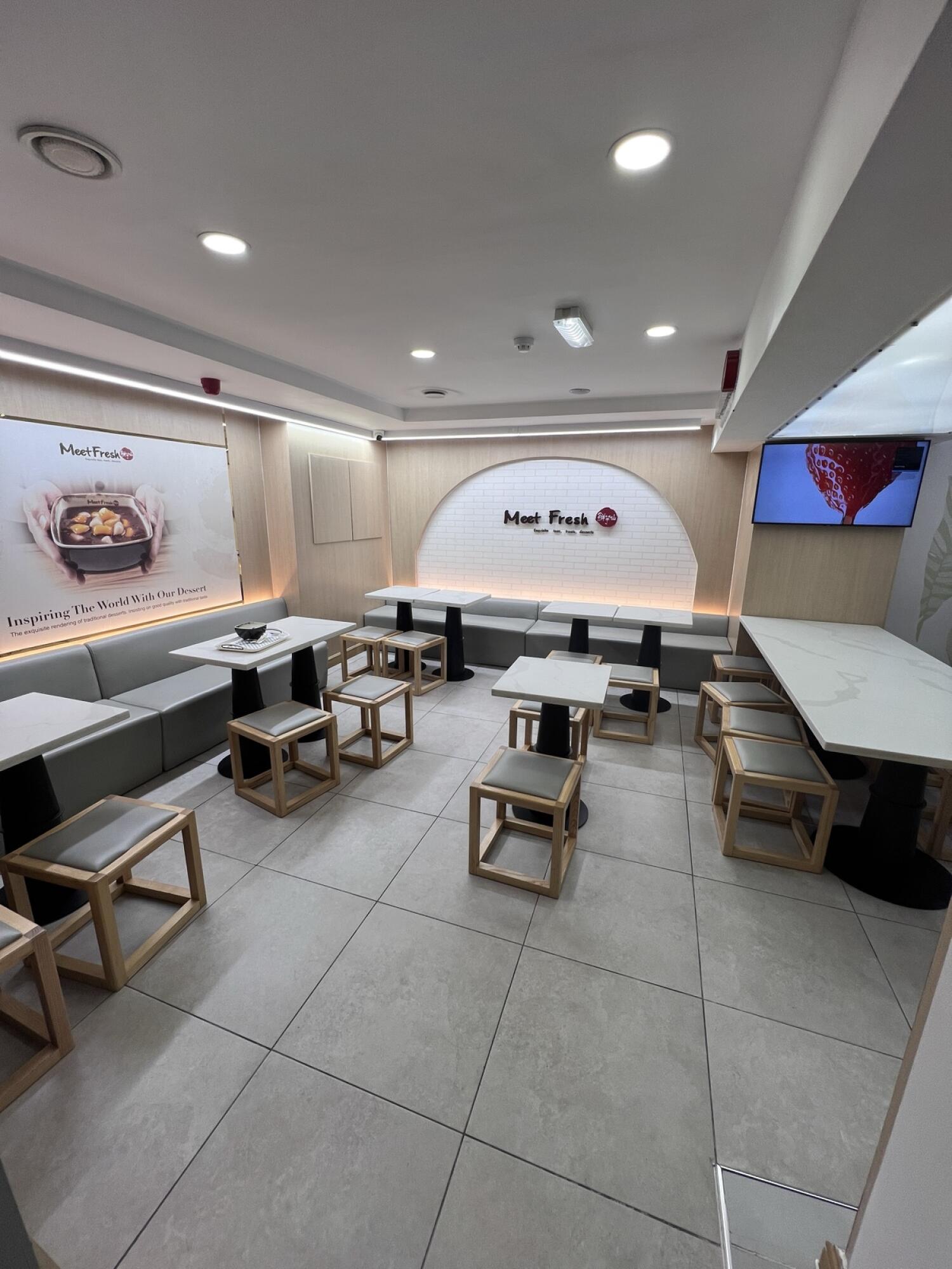 Half booth along left wall. Tiled floor with central tables. Long table and stools right.